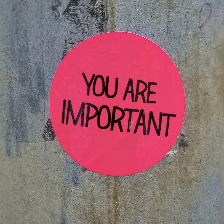 A round pink sticker on a wooden surface with bold black text reading “YOU ARE IMPORTANT.”