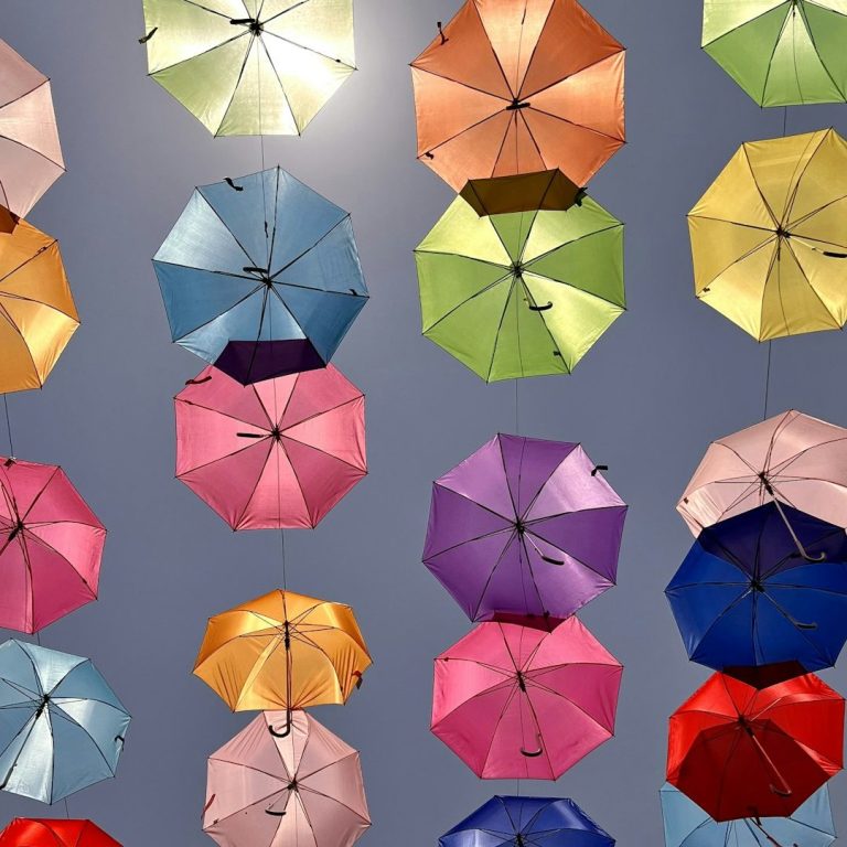 Brightly coloured umbrellas floating in the air against a purple background, symbolising diversity and inclusion.
